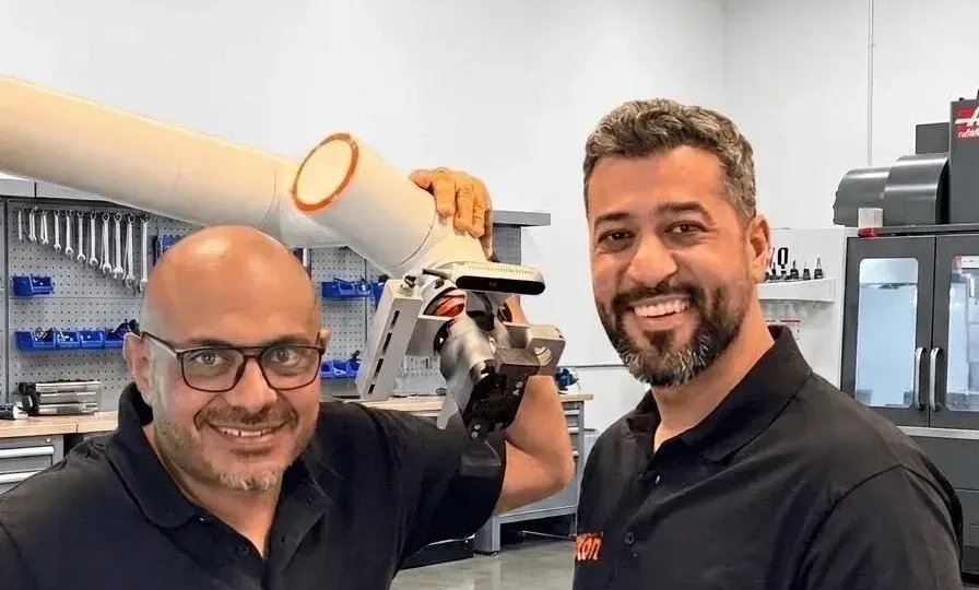 Axton Robotics co-founders Malak Mitch and Michael Nessim smiling next to a collaborative robot arm in the Axton Robotics CNC automation shop in San Diego, California